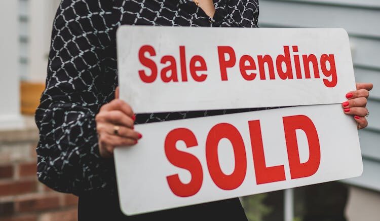 A woman holding Sale Pending and Sold signs.